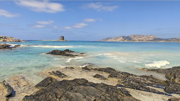 A coastal landscape with clear turquoise waters, rocky shorelines, and a distant tower. - Villa Blu with pool in Stintino – Sardinia (Punta de Su Turrione)