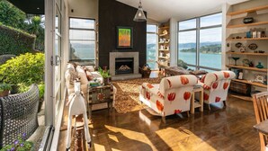 A spacious living room with a fireplace, large windows, and a view of the sea. - Roseneath Escape - Panoramic Harbour Views (Wellington)