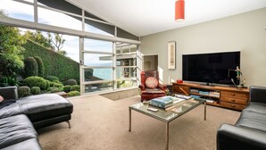 A modern living room with a large TV, comfortable seating, and a view of a landscaped garden. - Roseneath Escape - Panoramic Harbour Views (Wellington)