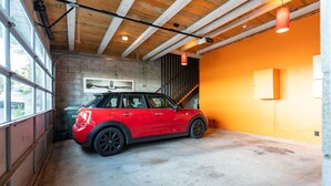 A red Mini Cooper parked in a garage with exposed wooden beams, a concrete floor, and an orange wall. - Roseneath Escape - Panoramic Harbour Views (Wellington)