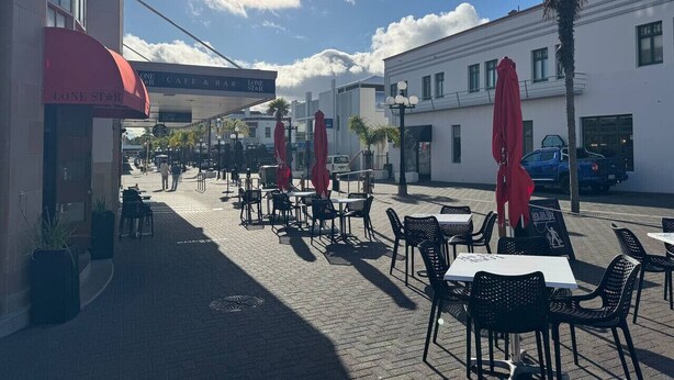 An outdoor cafe with tables and chairs, umbrellas, and a building with a sign. - Chic 2 Bedroom Apartment in Art Deco Napier (Napier)