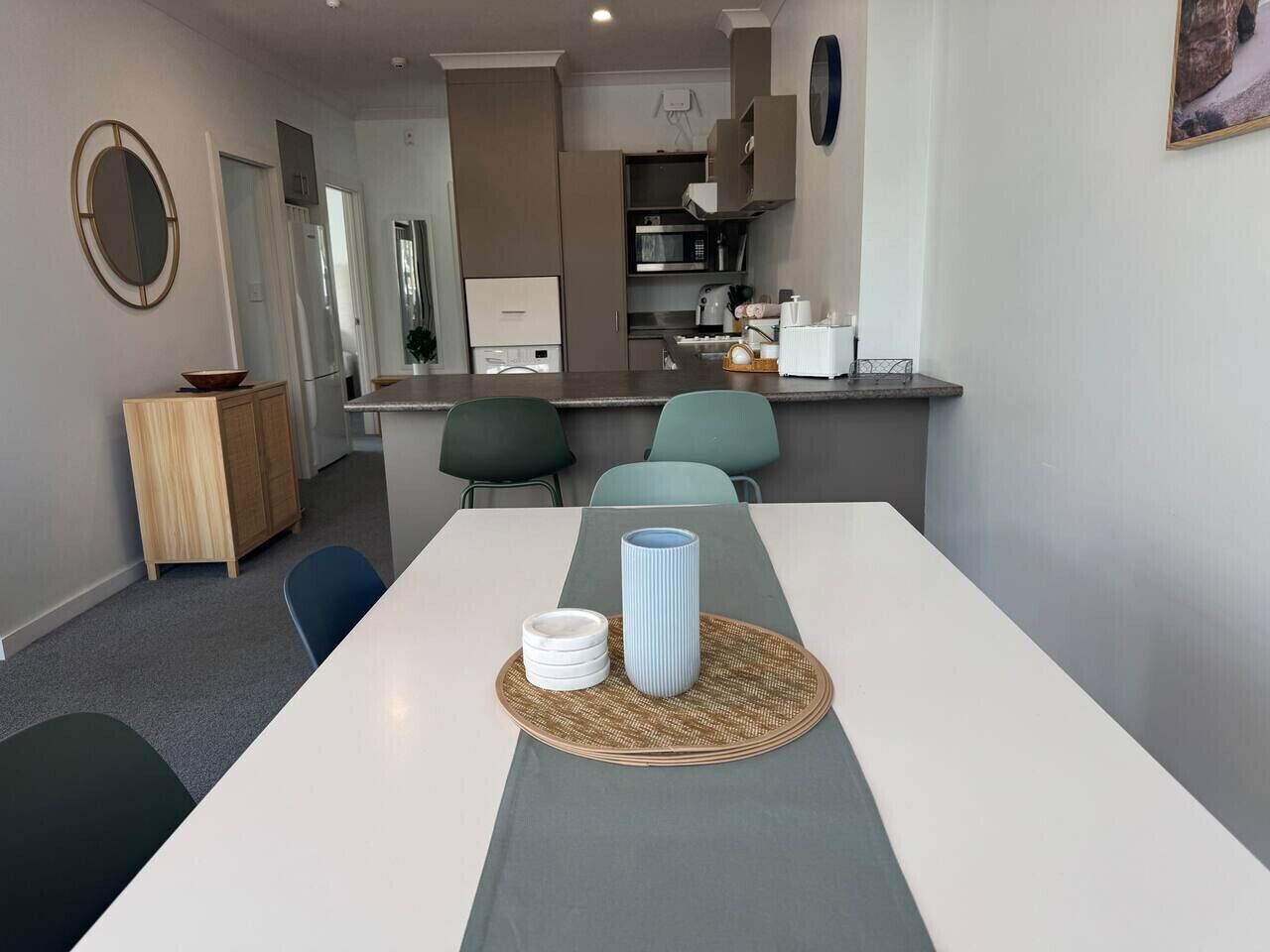 A modern kitchen with a central island, a dining area with a long table, and a seating arrangement with chairs.