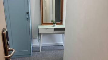A narrow hallway with a blue door, a white desk with a mirror, and a small plant.