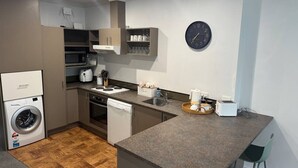 A compact kitchen with a washing machine, dishwasher, microwave, and a clock on the wall. - Chic 2 Bedroom Apartment in Art Deco Napier (Napier)