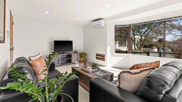 A modern living room with a flat-screen TV, leather sofas, a coffee table, and a large window offering a view of trees and a building. - Havelock North Heartbeat (Havelock North)