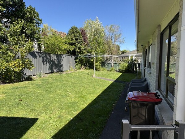 A backyard with a lawn, a fence, and a patio area with outdoor furniture.