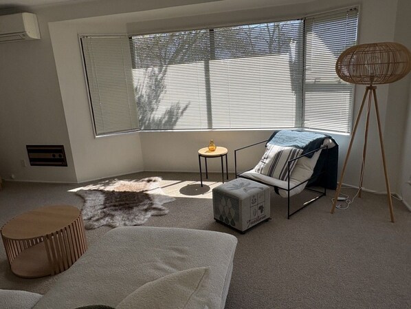 Ein Zimmer mit großem Fenster, einer Couch, einem kleinen runden Tisch und einer Stehlampe.