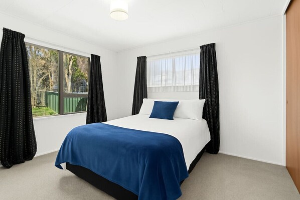 A bedroom with a bed, large windows, and curtains.
