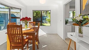 A dining area with a wooden table and chairs, a vase with flowers, and a view of a backyard through a window. - Havelock North Heartbeat (Havelock North)