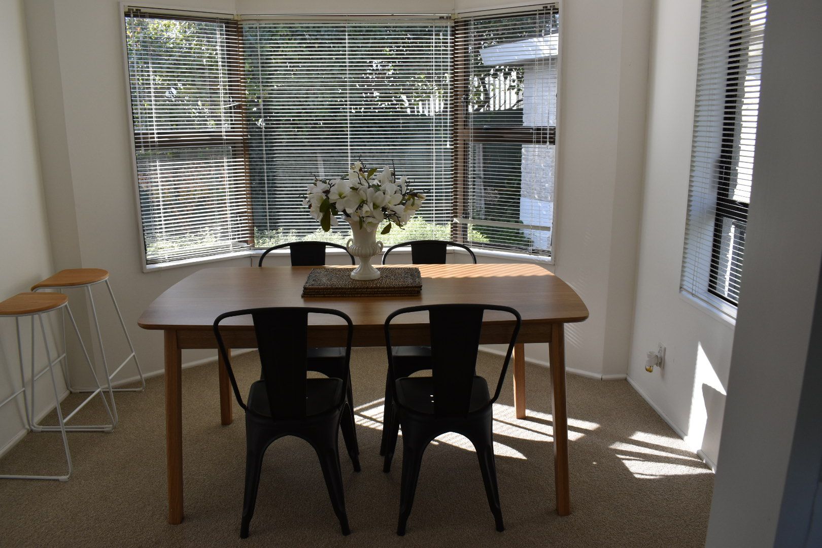 A dining area with a wooden table, four chairs, and a vase of flowers.
