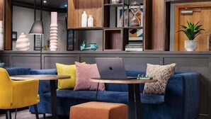 A modern living room with a blue sofa, yellow and pink cushions, a small table with a laptop, and a potted plant. - Holiday Inn LEEDS - WAKEFIELD M1, JCT.40 by IHG (Wakefield)