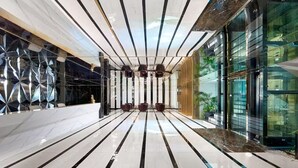 En modern entréhall med ett reflekterande golv, geometriska väggpaneler och en glasfasad.