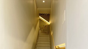Una stretta scala ben illuminata con gradini bianchi e una ringhiera a destra.