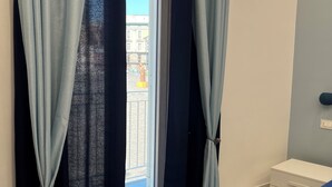 Una stanza con un balcone, un letto, un comodino e delle tende.