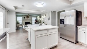 A modern kitchen with a central island, stainless steel appliances, and a dining area with chairs and a table. - Reston NEW Bright, Airy Home w/ In Ground Pool & Grill (Richardson)