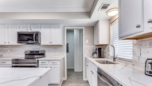 A modern kitchen with white cabinetry, a built-in microwave, a stove, and a large island with a sink. - Reston NEW Bright, Airy Home w/ In Ground Pool & Grill (Richardson)