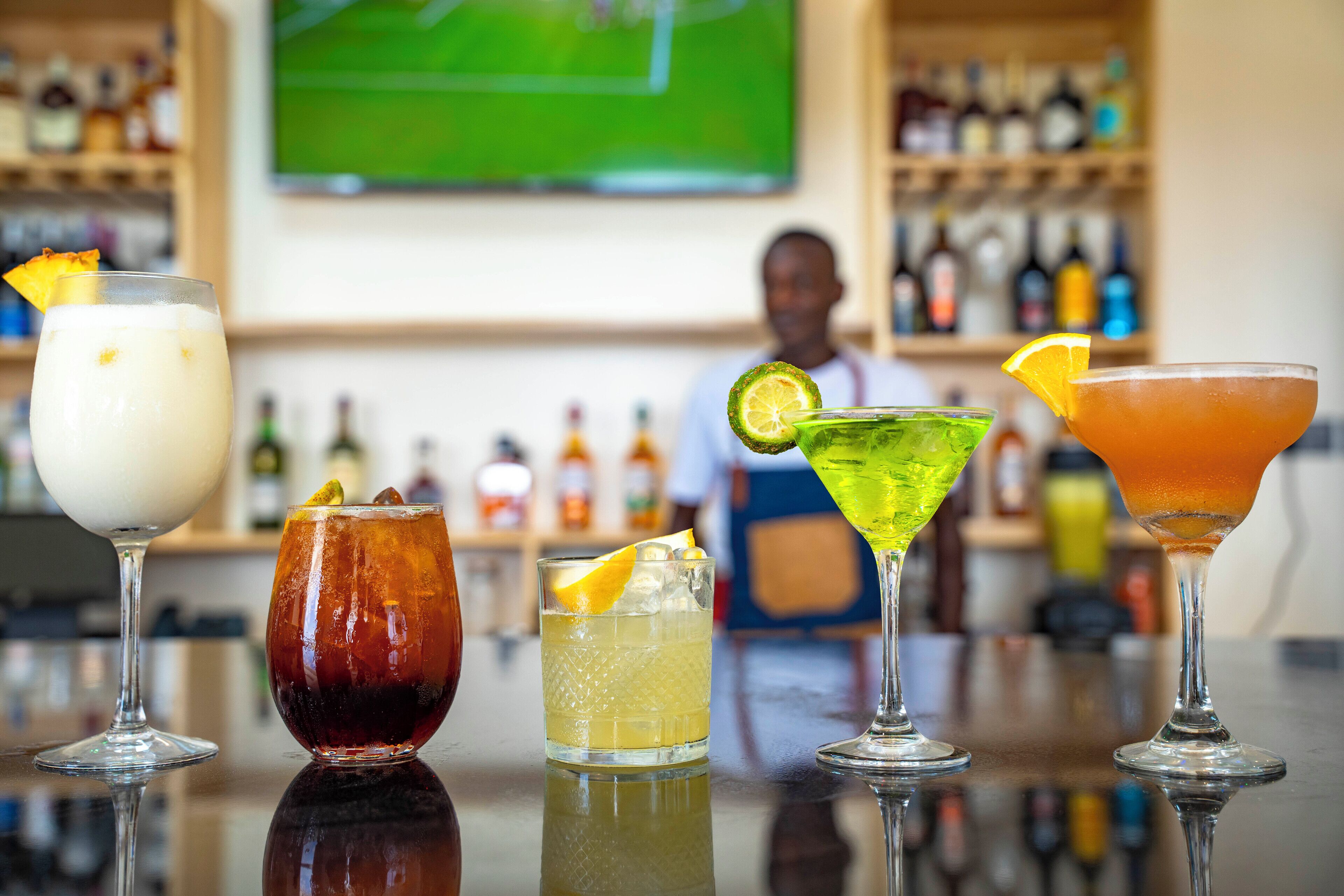 Un bar con diversos cócteles, un cantinero y estantes llenos de botellas de licores.