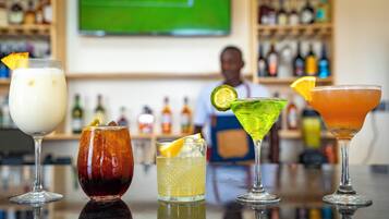 Un bar con diversos cócteles, un cantinero y estantes llenos de botellas de licores.