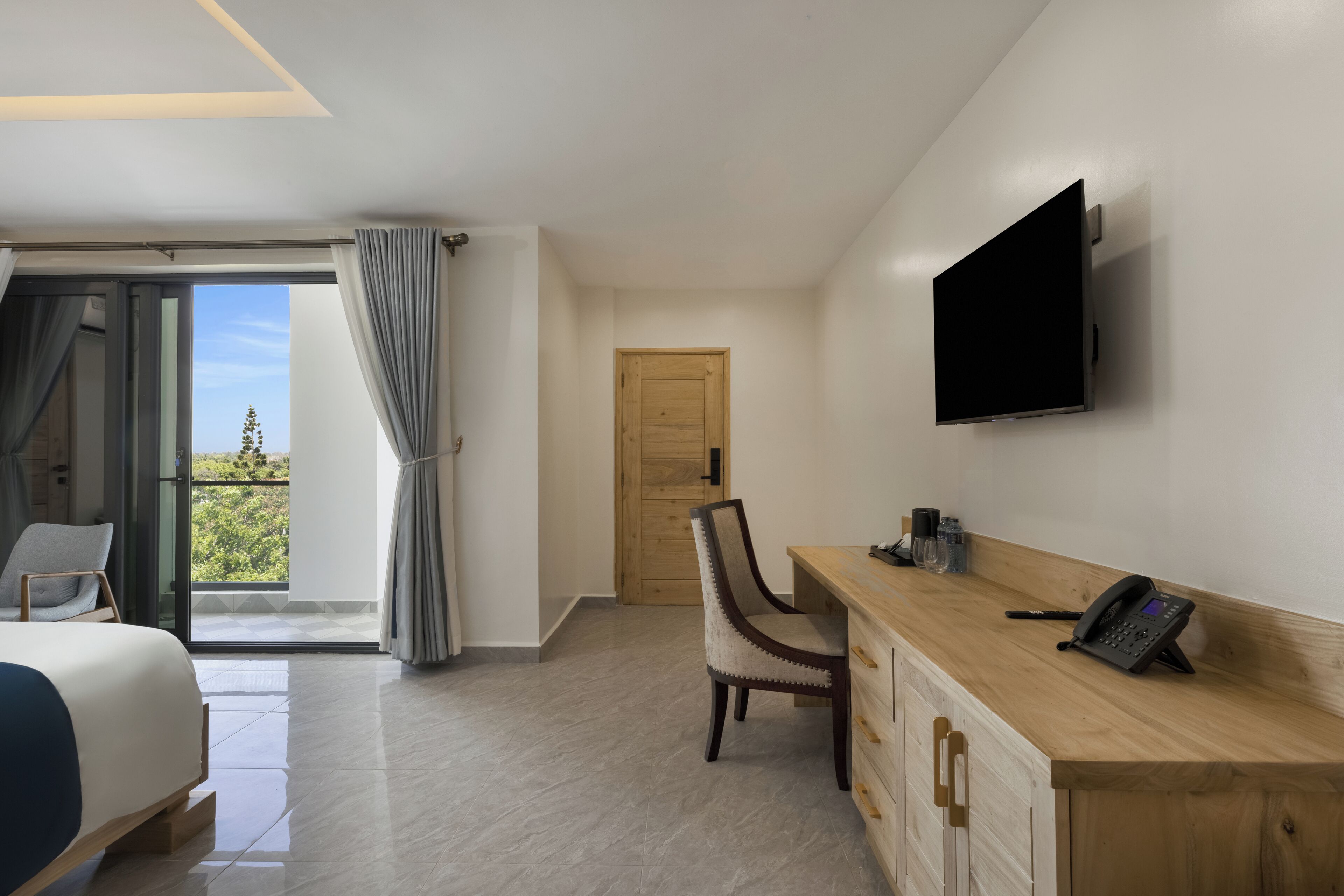 A modern hotel room with a bed, a desk with a telephone, a chair, and a TV mounted on the wall.