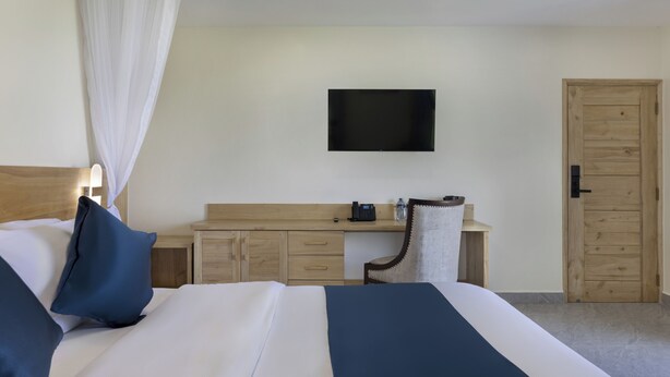 A hotel room with a bed, a desk, a chair, a television, and a door. - Marikeka Hotel (Diani Beach)