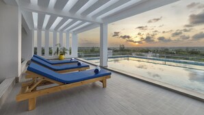 Eine Dachterrasse mit Holzliegen und Blick auf den Sonnenuntergang über dem Wasser.