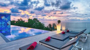 Une piscine à débordement avec des chaises longues et une vue imprenable sur le coucher de soleil.