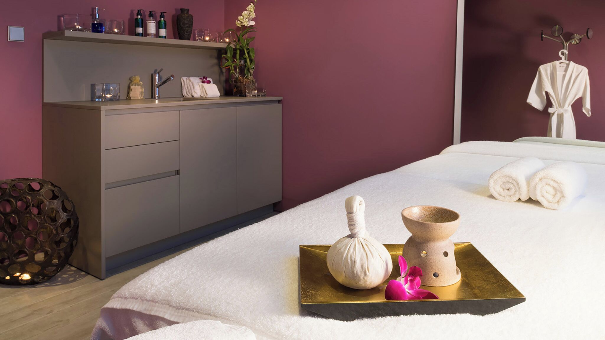 A modern hotel room with a large bed, a minibar, a vanity with toiletries, and a decorative plant.