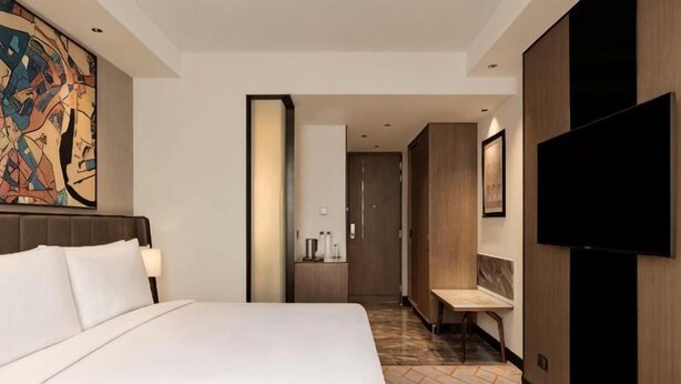 A hotel room with a large bed, a television, a bathroom, and a hallway. - Crowne Plaza Lucknow by IHG (Chak Kajehra)