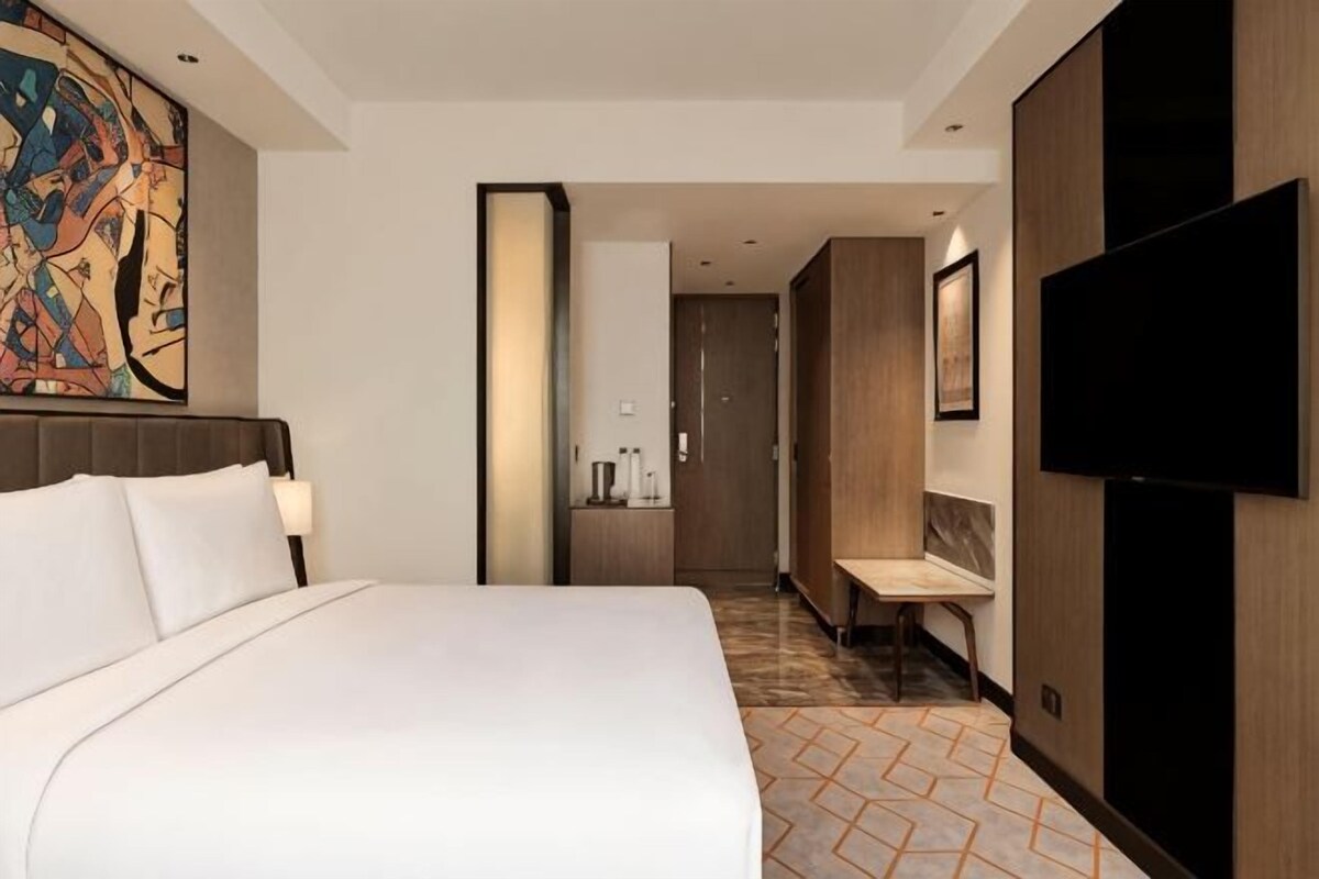 Una habitación de hotel con una cama grande, televisión, baño y pasillo.