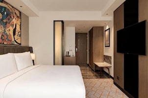 Una habitación de hotel con una cama grande, televisión, baño y pasillo.