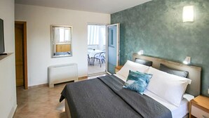 Quarto com cama, mesas de cabeceira, radiador, janela e vista para uma sala de jantar.