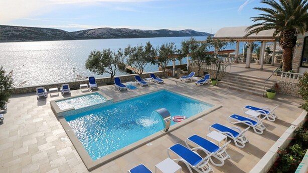 Área da piscina com vista para o mar e montanhas, rodeada por espreguiçadeiras e um caminho de pedra.