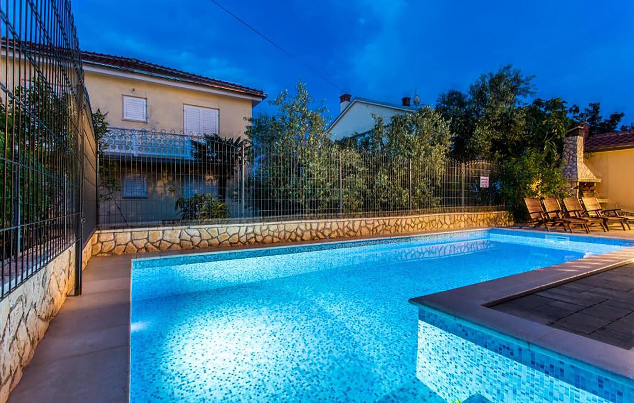 A swimming pool with a stone border, surrounded by a fence and trees.