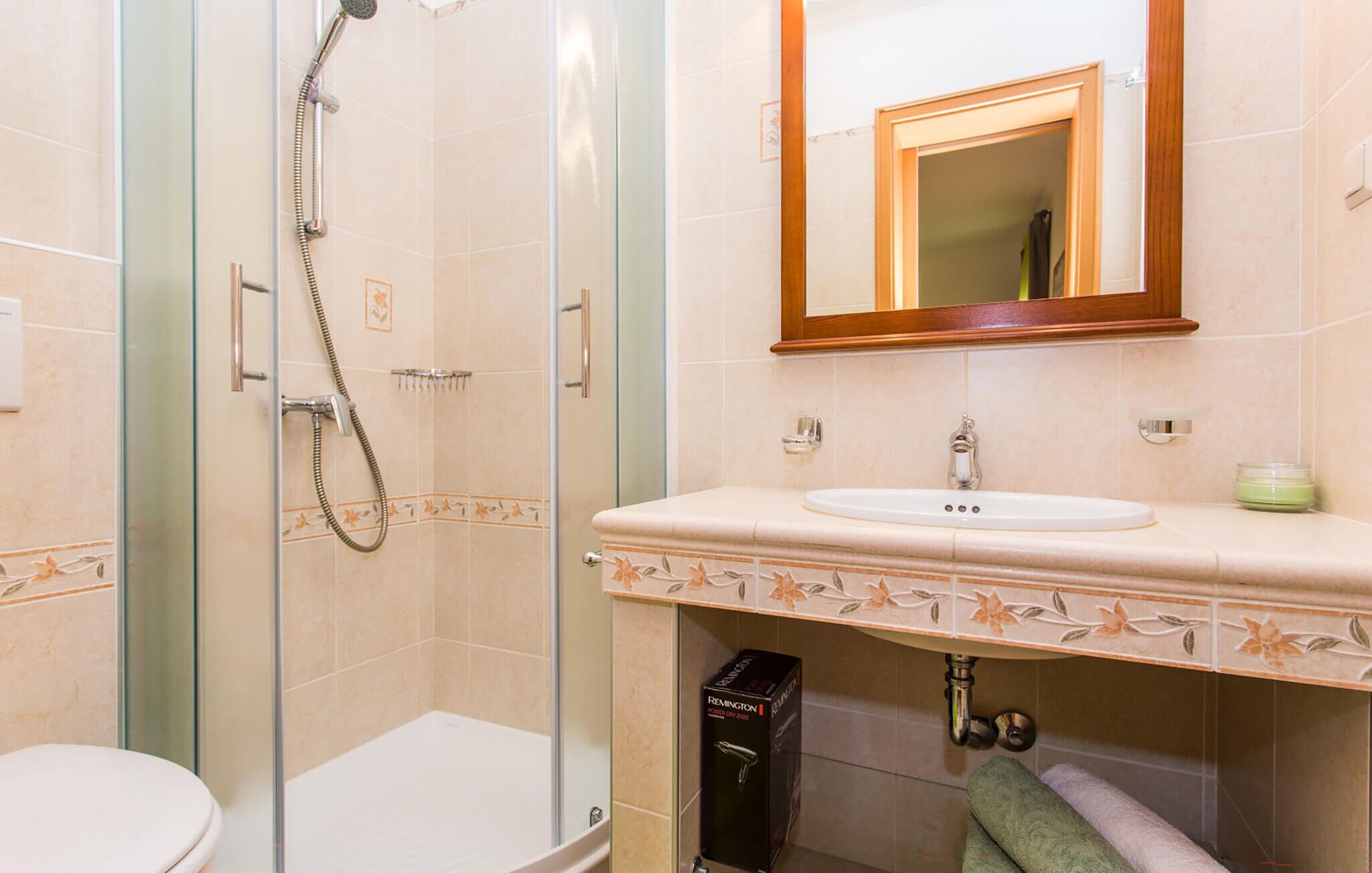 Un baño con ducha de vidrio, un lavamanos blanco y un espejo sobre él.
