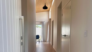A hallway with wooden flooring, white walls, and a ceiling with wooden beams. There is a door on the right and a door with a handle on the left. - Mapua Haven – Contemporary New Home (Māpua)