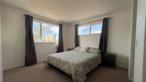 A bedroom with a large bed, two bedside tables, and a window with curtains. - Mapua Haven – Contemporary New Home (Māpua)