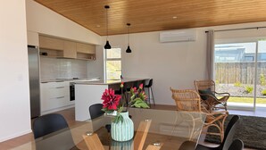 A modern kitchen with wooden cabinets, a dining area with a glass table, and wicker chairs. - Mapua Haven – Contemporary New Home (Māpua)