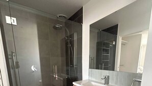 A modern bathroom with a glass shower enclosure, a white sink, and a wooden vanity. - Mapua Haven – Contemporary New Home (Māpua)