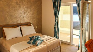 Un dormitorio con cama, almohadas, una colcha y vistas al exterior por un ventanal corredero.