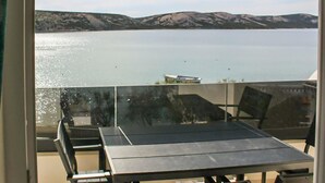 Un balcón con mesa y sillas que da a un lago tranquilo y montañas lejanas.