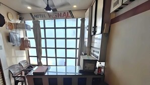 Un mostrador de recepción en un hotel con un ventanal amplio, un ventilador de techo y un letrero encima del mostrador.