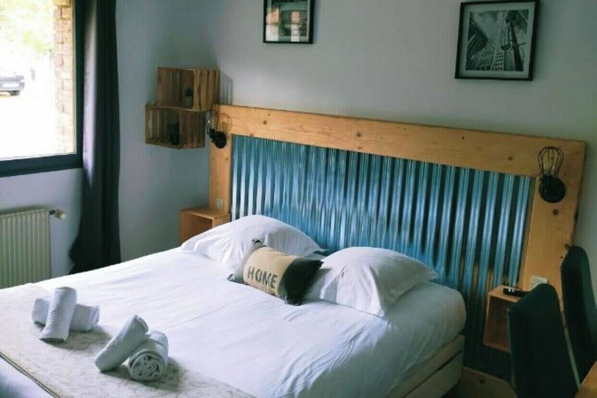 A hotel room with a bed, a wooden headboard, a nightstand, a chair, and a window with curtains.