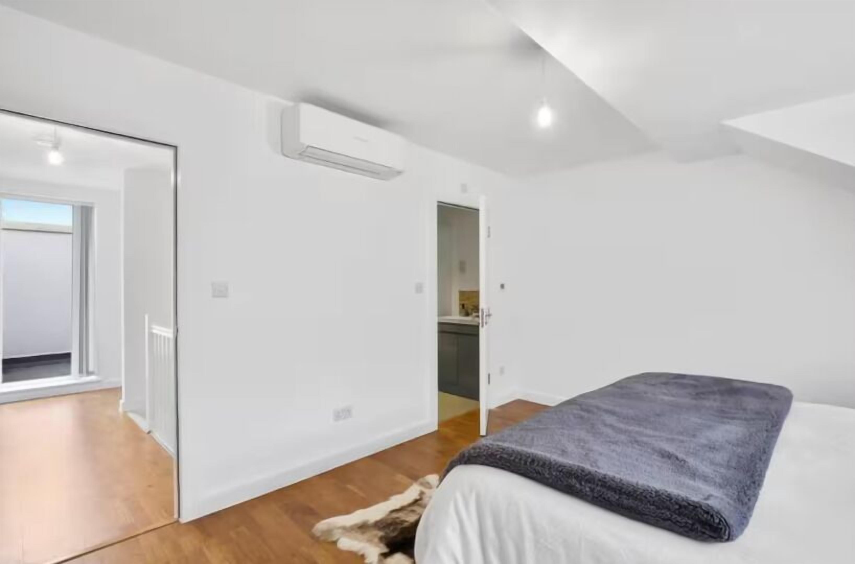A modern bedroom with a large bed, a white wardrobe, and a visible kitchen area.