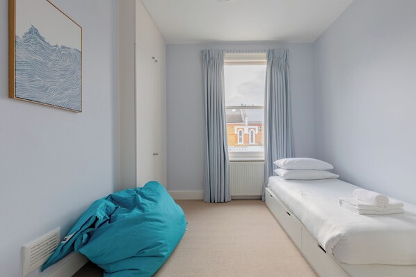 A bedroom with a bed, a window with curtains, a radiator, and a wall-mounted picture.