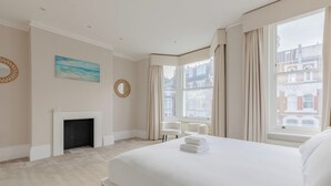 Hotellihuone, jossa on suuri sänky, takka, ikkunasta avautuva näkymä rakennuksiin ja seinällä oleva taulu.