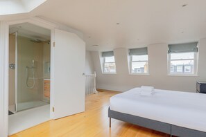 Un dormitorio con cama, ducha y vistas a edificios a través de ventanas.