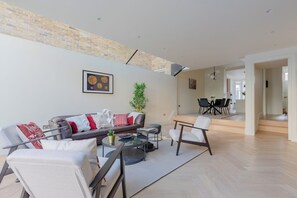 A modern living room with a sofa, chairs, a coffee table, and a dining area with a table and chairs. - Impeccably Designed 5BD Family Home in West London (Greater London)