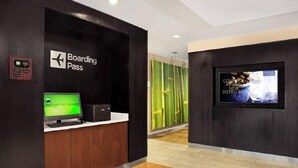 Un hall d’hôtel moderne avec un panneau indiquant « Carte d’embarquement », un écran de télévision et une publicité pour un « nouveau bar-bistro ».