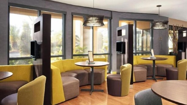 Un espace de détente moderne avec des sièges aux couleurs jaune et marron, de grandes fenêtres et des luminaires suspendus.