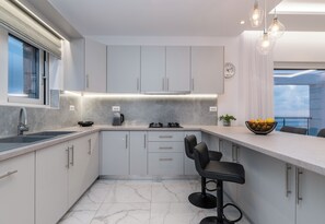 A modern kitchen with a marble countertop, built-in cabinets, a gas stove, and a dining area with bar stools. - Villa Orizzonte- First Floor Apartment (Zakynthos)